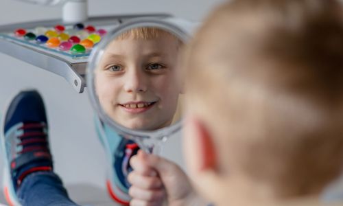 Junger Patient der Kinderorthopädie bei Dr. Ute Pilot guckt in einen Spiegel und begutachtet seine Zähne